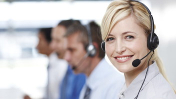 Pretty customer services operator smiling at you with colleagues in background - copyspace